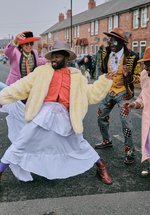A photograph of five people in a circle dressed in colourful, formal outfits. 