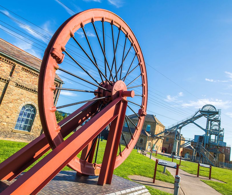A large metal wheel with a bigger metal structure and wheel in the background