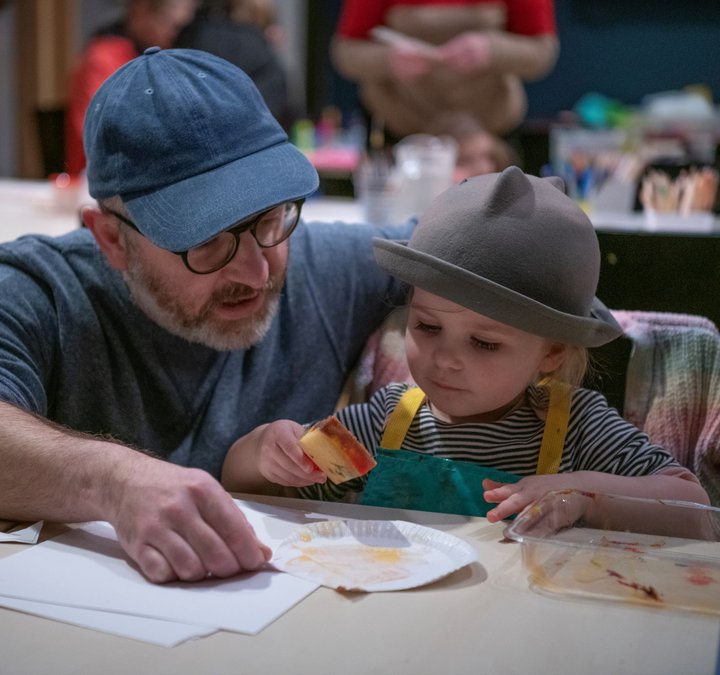 A photograph of a dad helping his young daughter with her arts and crafts.