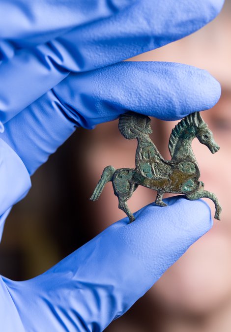 A person is holding a small horse brooch found at Arbeia.