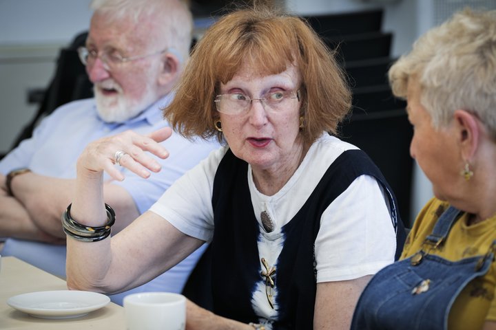 A photograph of three people conversing around a table.