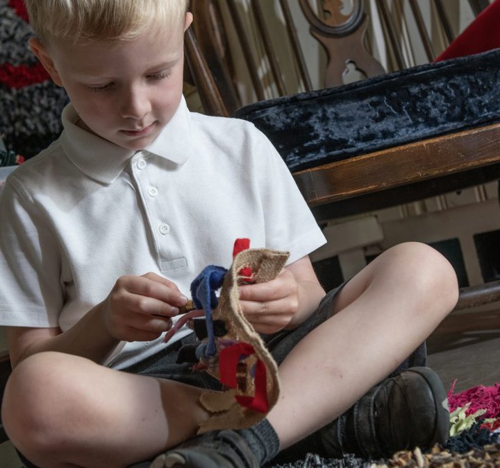 A child is sat on the floor making a proggy mat with craft materials