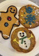 A photograph of three cookies: one gingerbread man, one with a snowman decoration, and one with snowflakes.