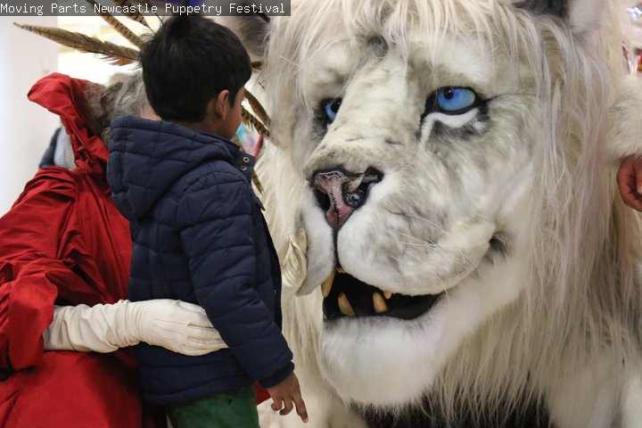 An adult and a child are looking at a large snow lion puppet