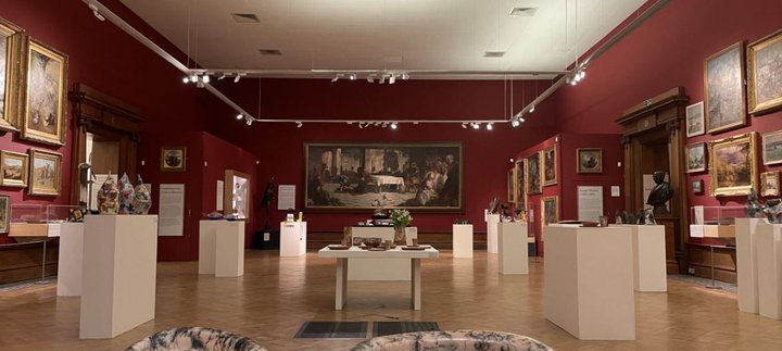 A display of glass and ceramic objects on white plinths in a gallery space.