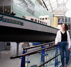 Two young adults walk alongside the ship Turbinia