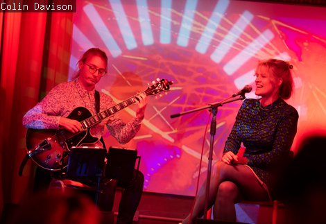 Photograph of 2 musicians performing on a colourful lit stage