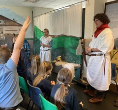 Adults dressed as Romans talking to a class of school children
