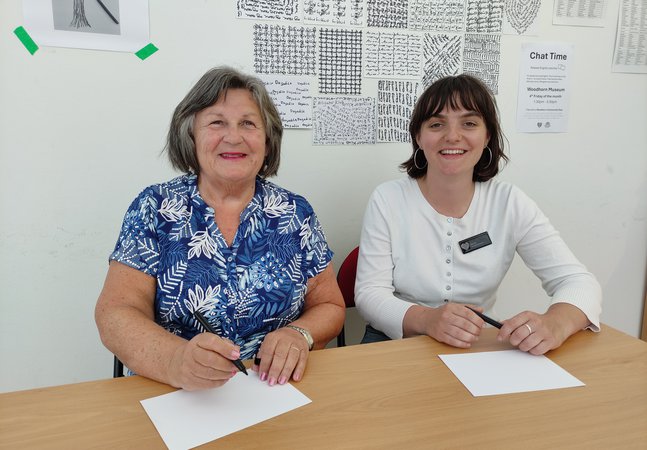 Two Chat Time Volunteers sitting at a desk and smiling at Woodhorn Museum 