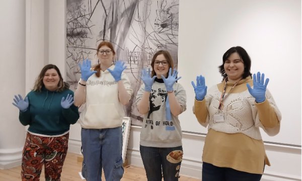 4 young adults in an art gallery, wearing gloves and smiling. 4 young adults in an art gallery, wearing gloves and smiling.