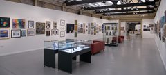 A gallery space with artworks on the walls and glass display cases filled with pottery and sculpture