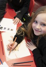 Girl sitting at a red table colouring in some paper