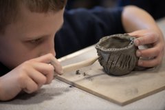 Young child using a pointed tool to inscribe small clay pot