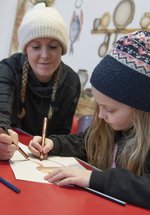 Woman and young girl wearing woolly hats sitting at a table doing a craft activity