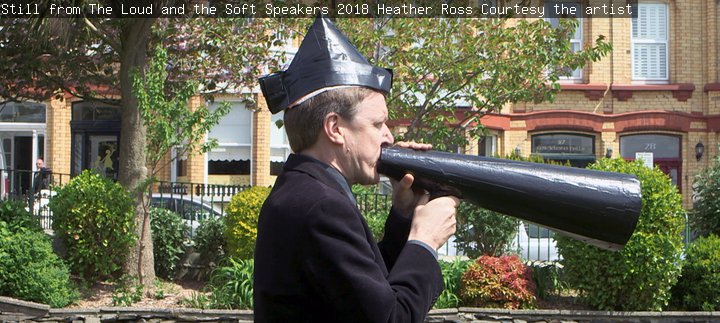 Still from a film. A man talking into a loud speaker.