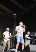 Band performing on stage with instruments and microphones, colorful lights in the background.