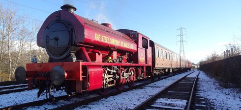 Red steam locomotive pulling passenger carriages on snow covered railway