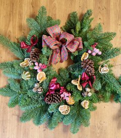 A photograph of a Christmas wreath decorated with dried oranges, pinecones, ribbons, and other decorations.