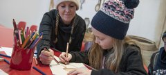 Woman and young girl wearing woolly hats sitting at a table doing a craft activity