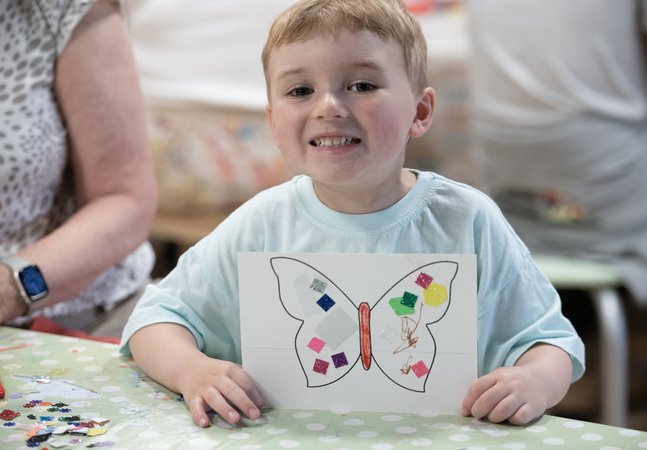 small boy smiles and hold up picture of butterfly