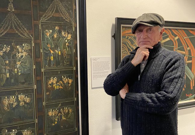 Bob Olley standing in front of his paintings in South Shields Museum