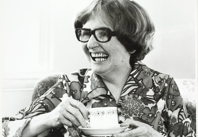 Dame Catherine Cookson laughs holding a cup of tea