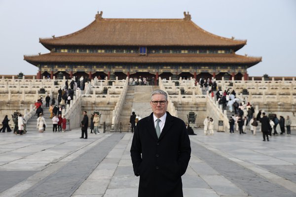 The Prime Minister stands in the foreground with a large traditional Chinese building in the background with a large two-tiered roof with upturned eaves.