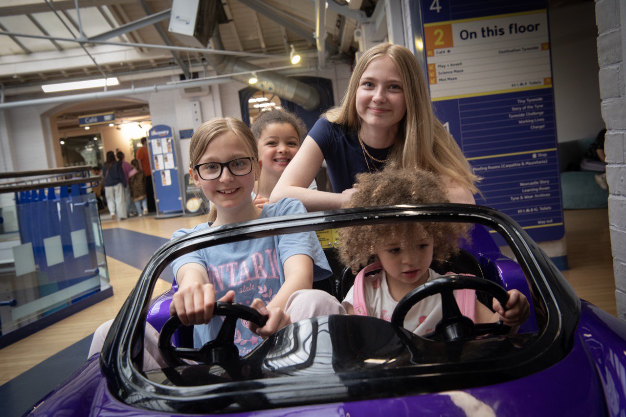 Four children playing in a car simulator ride.