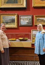 Two people standing smiling besides a glass display case in a gallery