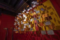 Art installation featuring hanging gold squares and drawings