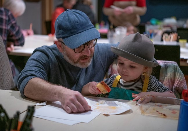 A photograph of a dad helping his young daughter with her arts and crafts.