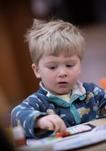 A child with short blonde hair sitting at a table and taking part in a craft activity