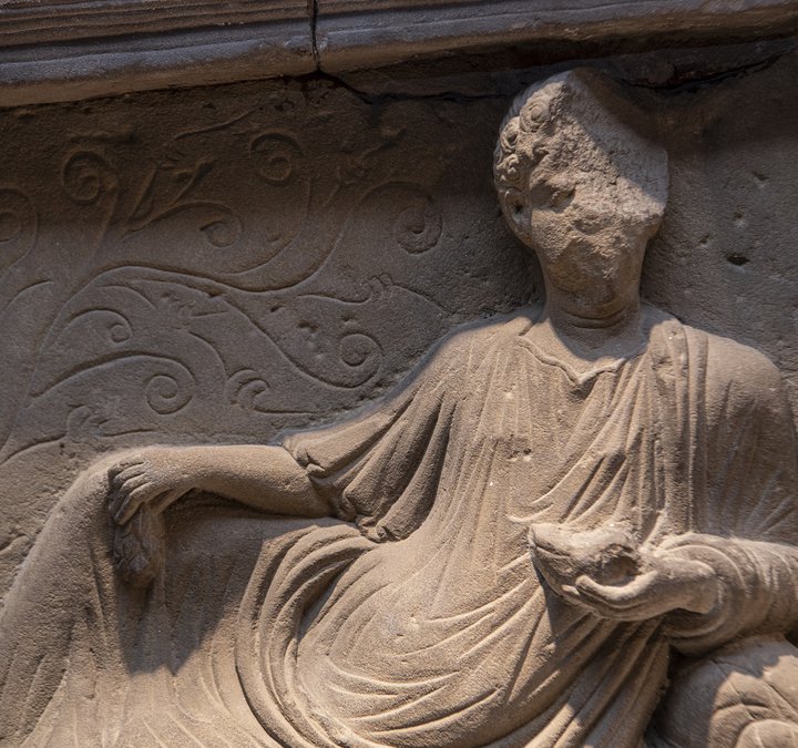 Close up of stone tombstone showing man reclining.