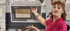 A woman gestures extravagantly to an image of a microwave