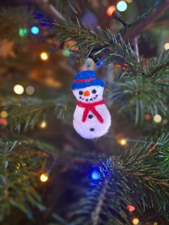 A photograph of a needle felted snowman Christmas decoration hanging on a Christmas tree.