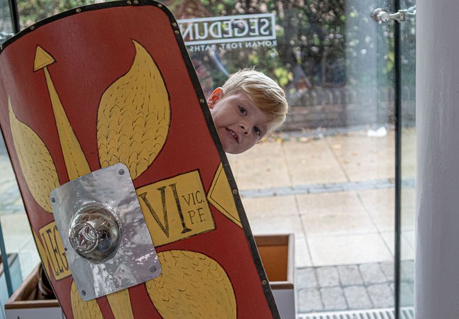 Young boy peeping out from behind a Roman style shield in the shop