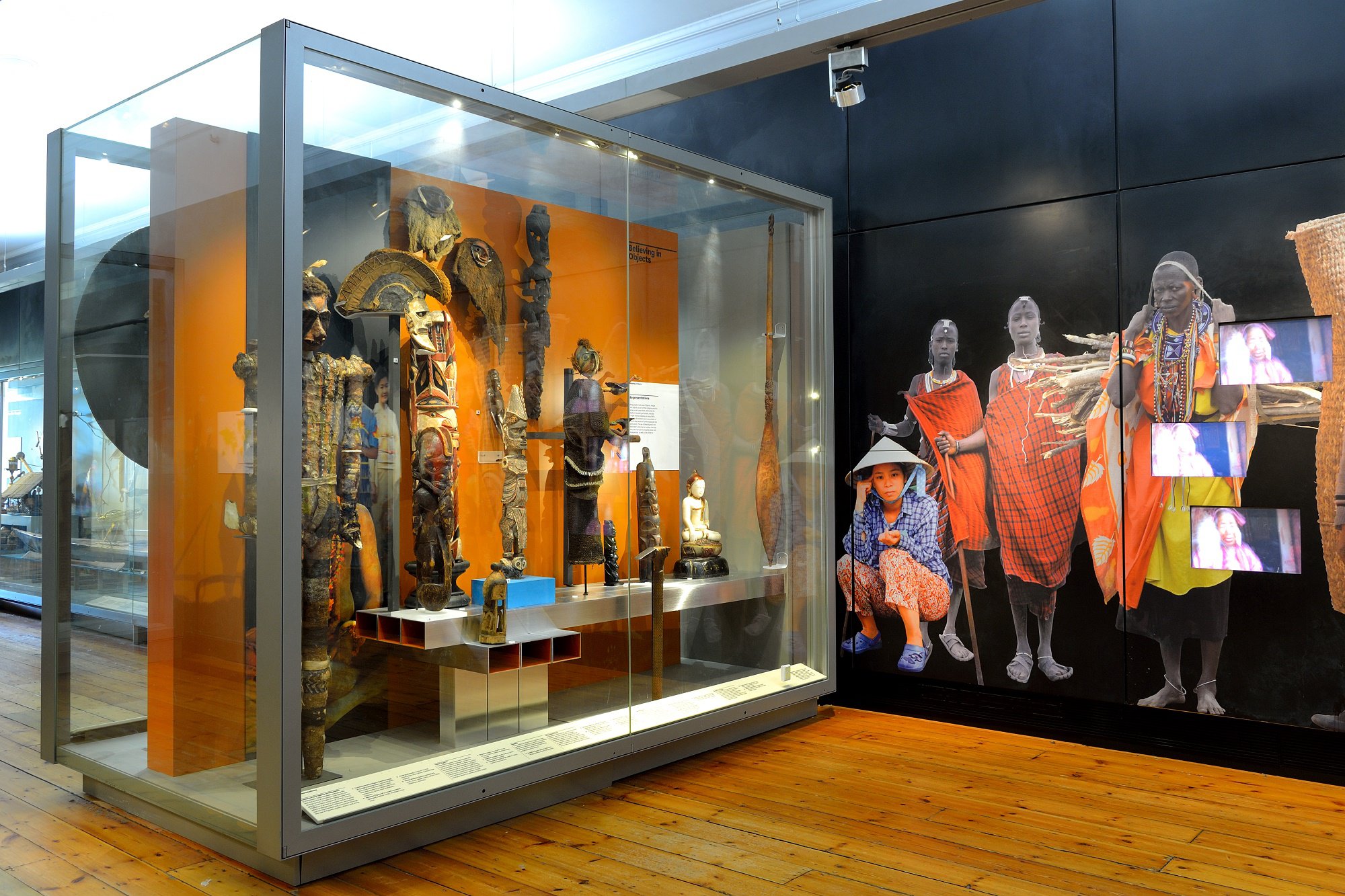 A large glass display case filled with ethnographic items. There is a graphic of Maasai women on the wall nearby.
