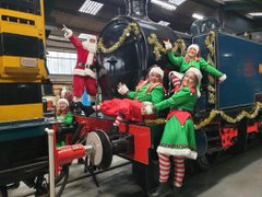 People dressed up as Christmas elves and Santa Claus standing on a blue locomotive