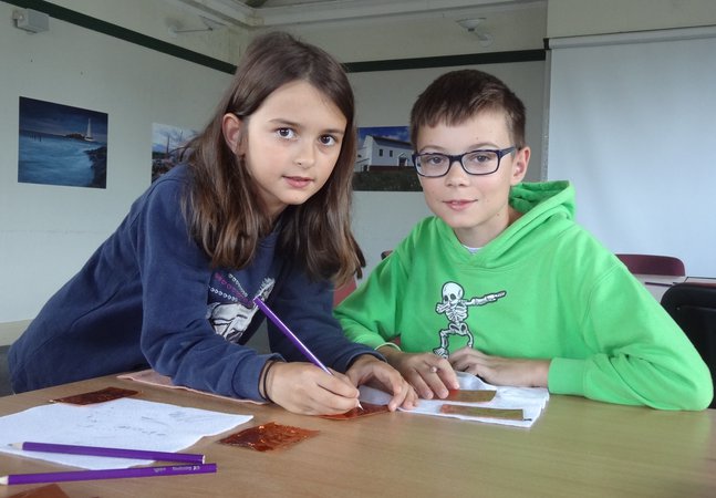 A boy and a girl embossing designs onto a copper sheet 
