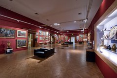 A photograph of the interior of the Shipley Art Gallery. The walls are red and there are many paintings on the walls in gold frames.