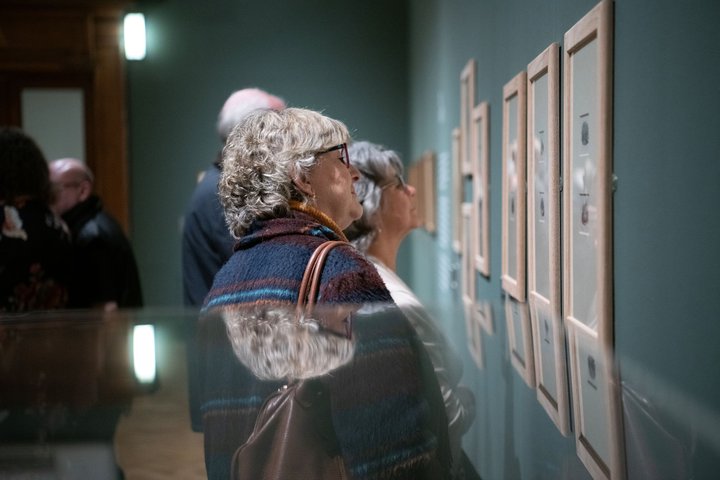 A woman looking at prints on a wall in a frame.