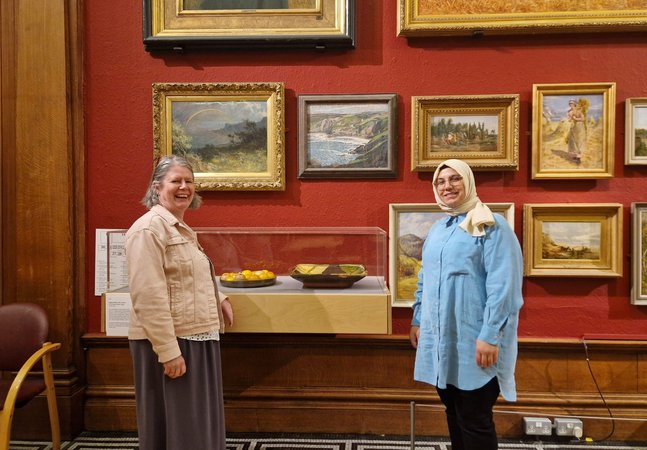 Two people standing smiling besides a glass display case in a gallery