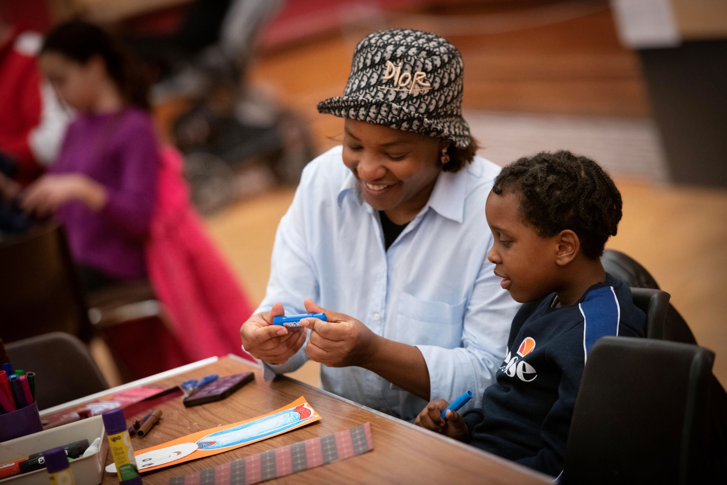 A woman and child sit at a table covered with craft materials A woman and child sit at a table covered with craft materials