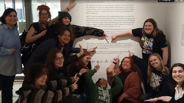 A group of young adults point and smile next to an interpretation panel. A group of young adults point and smile next to an interpretation panel.