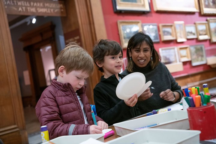 A photograph of a woman and two children crafting.