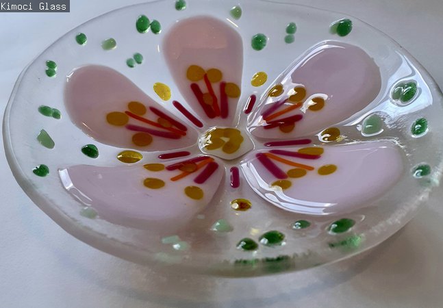 A photograph of a clear glass bowl with a pink flower.