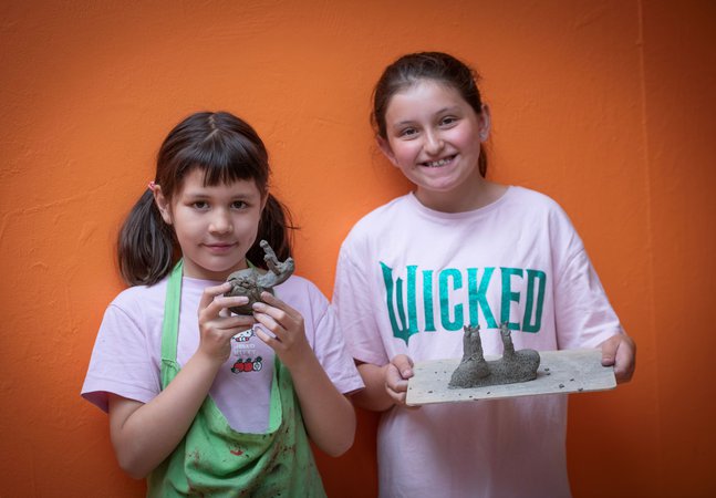 Two girls holding up their clay art projects.