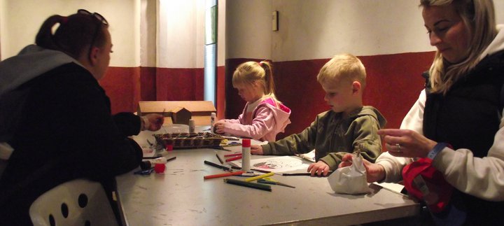 Two adults and two children sat at a table with pens and paper making crafts in the Roman Gallery