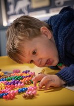 A child leans over a table and plays with a set of colourful  atom shaped toys