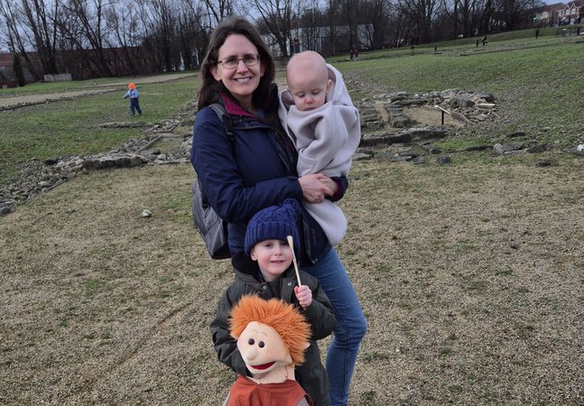 A woman holding a baby while a young child holds a soft toy on the fort site
